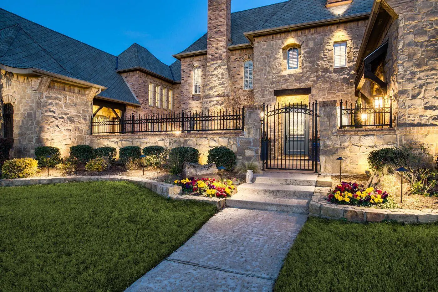 Stone home and planting beds illuminated at dusk
